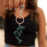 Del-Sol-Color-changing-Metal-Dolphin-Keychain--Silver-to-Blue dangling from a model's hand,.